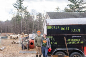 Kelly and her husband, Josh, posing in front of their livestock trailer with animals in the background.