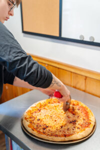 A close up image of a hand cutting a cheese pizza with a slicer.