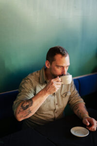 Owen Miller sipping coffee out of a white mug at local business, MUSE.