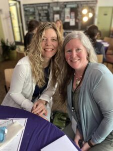 An image of two white women sitting at a purple table and smiling.