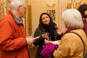 A young BIPOC woman and two older white individuals talking at a pitch event.