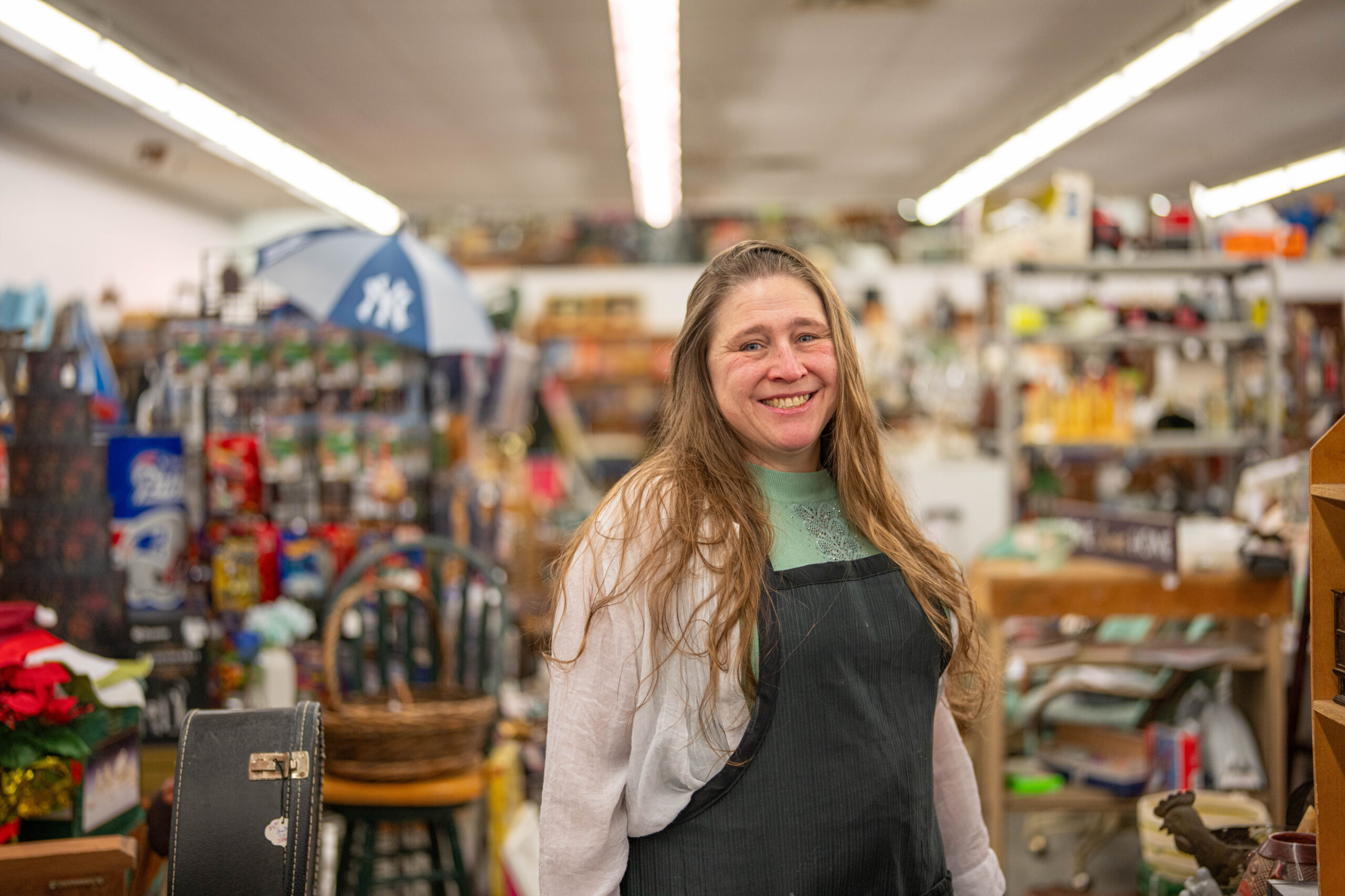 A white woman wearing an apron and standing in front of store shelves