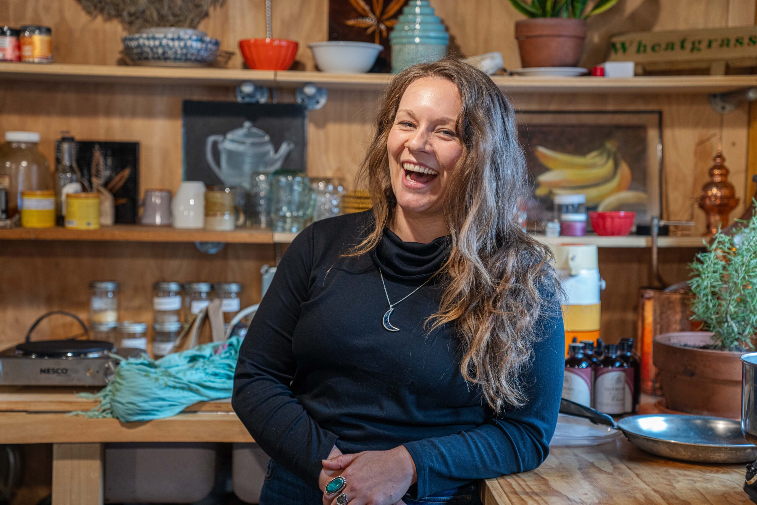 A white woman smiling in front of tea shop shelves.