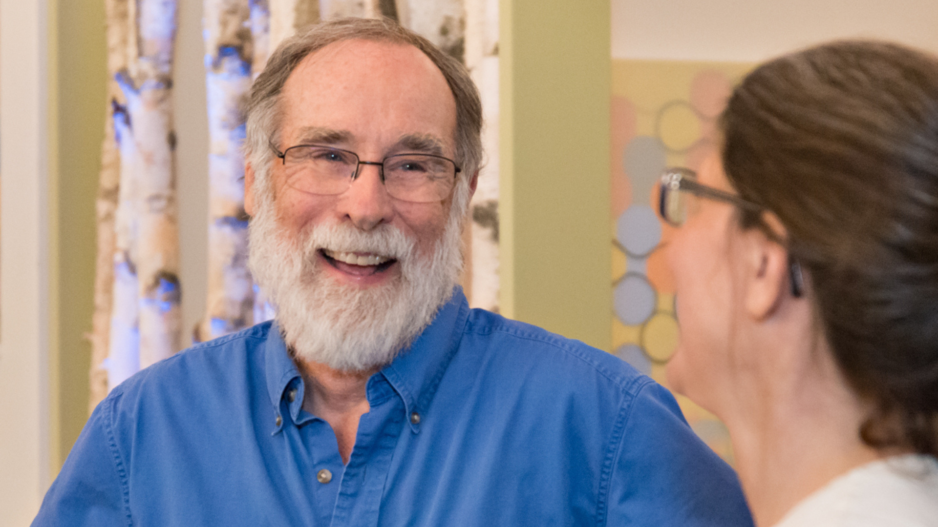 An older white man smiling and talking with a white woman.